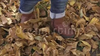 一个穿着棕色靴子和蓝色牛仔裤的一岁小男孩在秋天的公园里学习走路，全身是黄色的